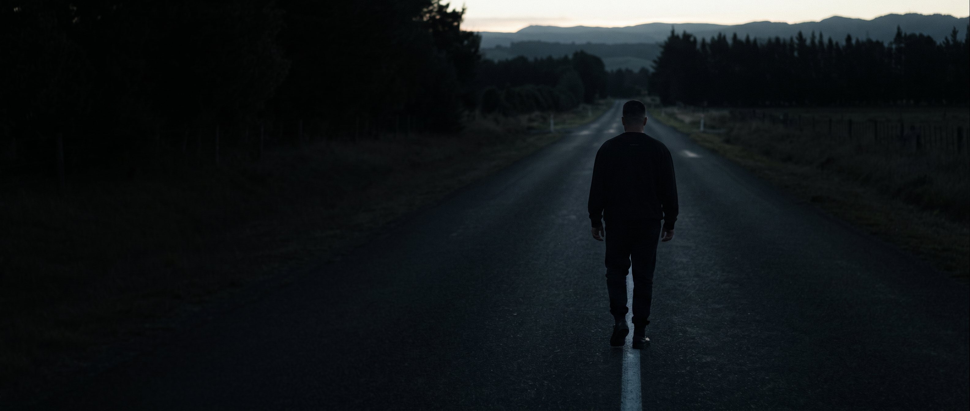 A man walking out through a dark doorway into low light, back to camera.
