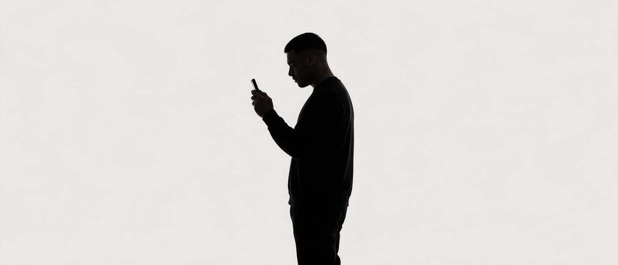 Silhouette standing, reading a phone held up at arm's length.