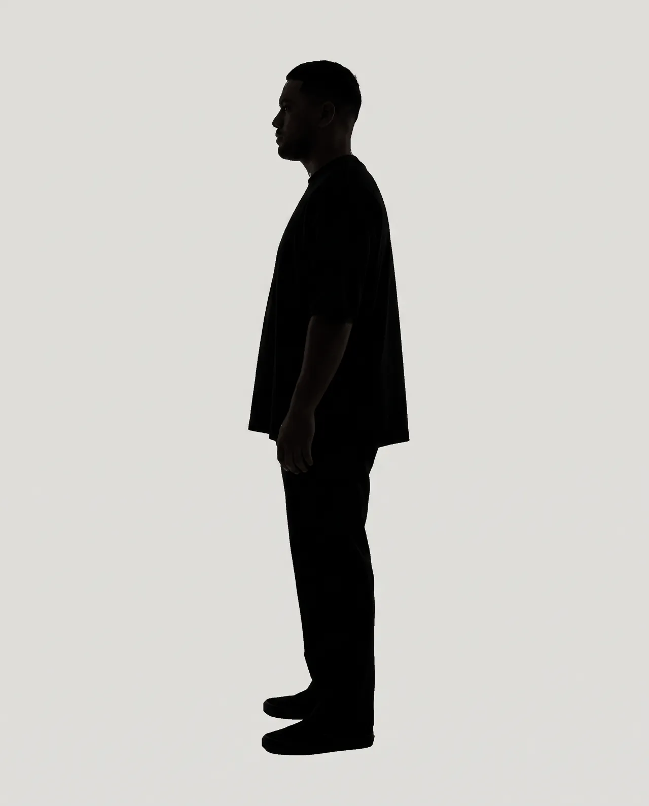 Dark silhouette of a man standing in profile, arms at his sides, on flat grey.