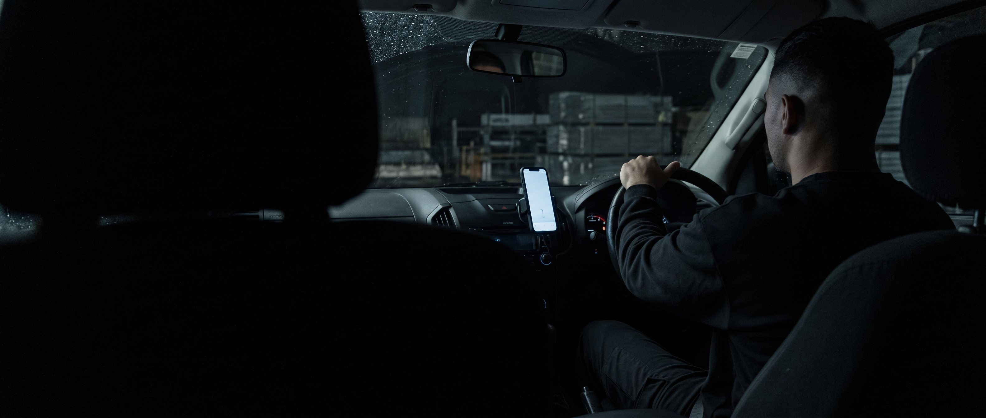 A man holding a phone in a dark workshop doorway, back to camera.