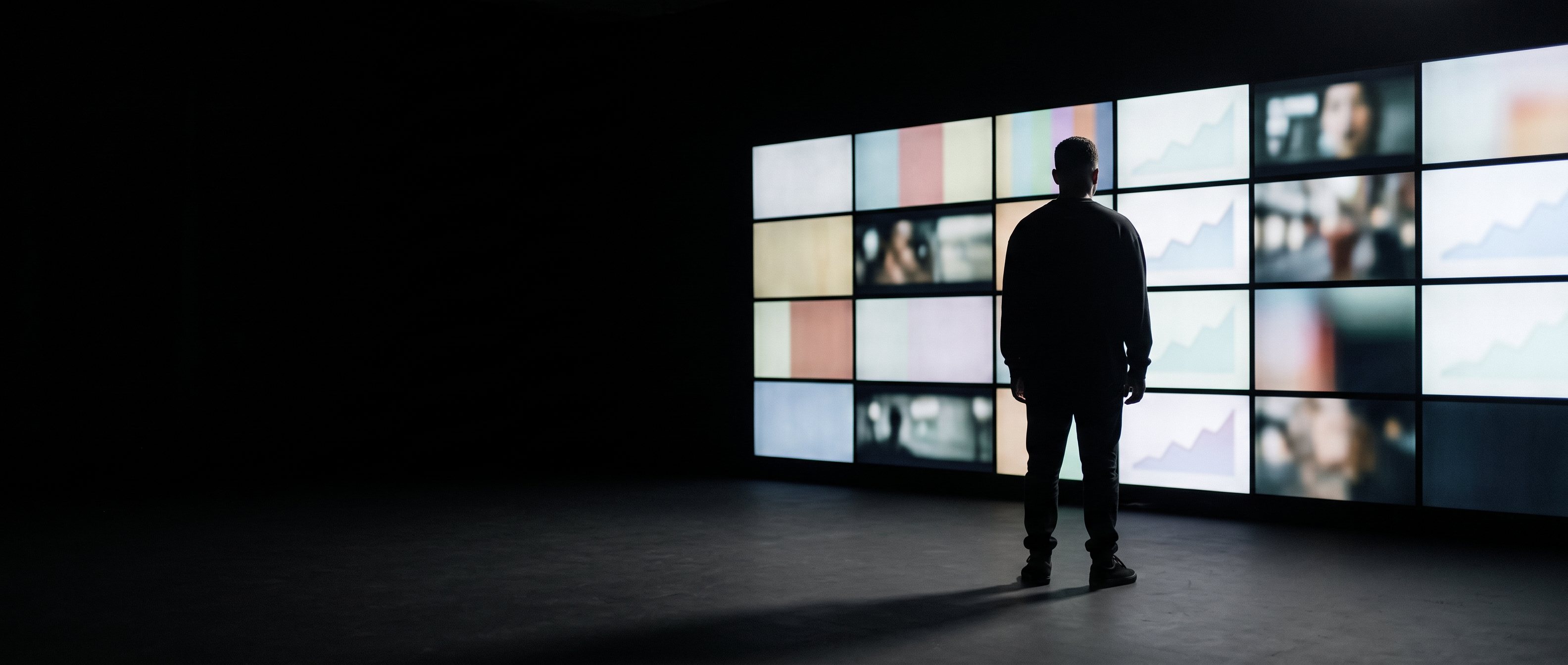 A man at a desk late at night lit by a single screen, back to camera.
