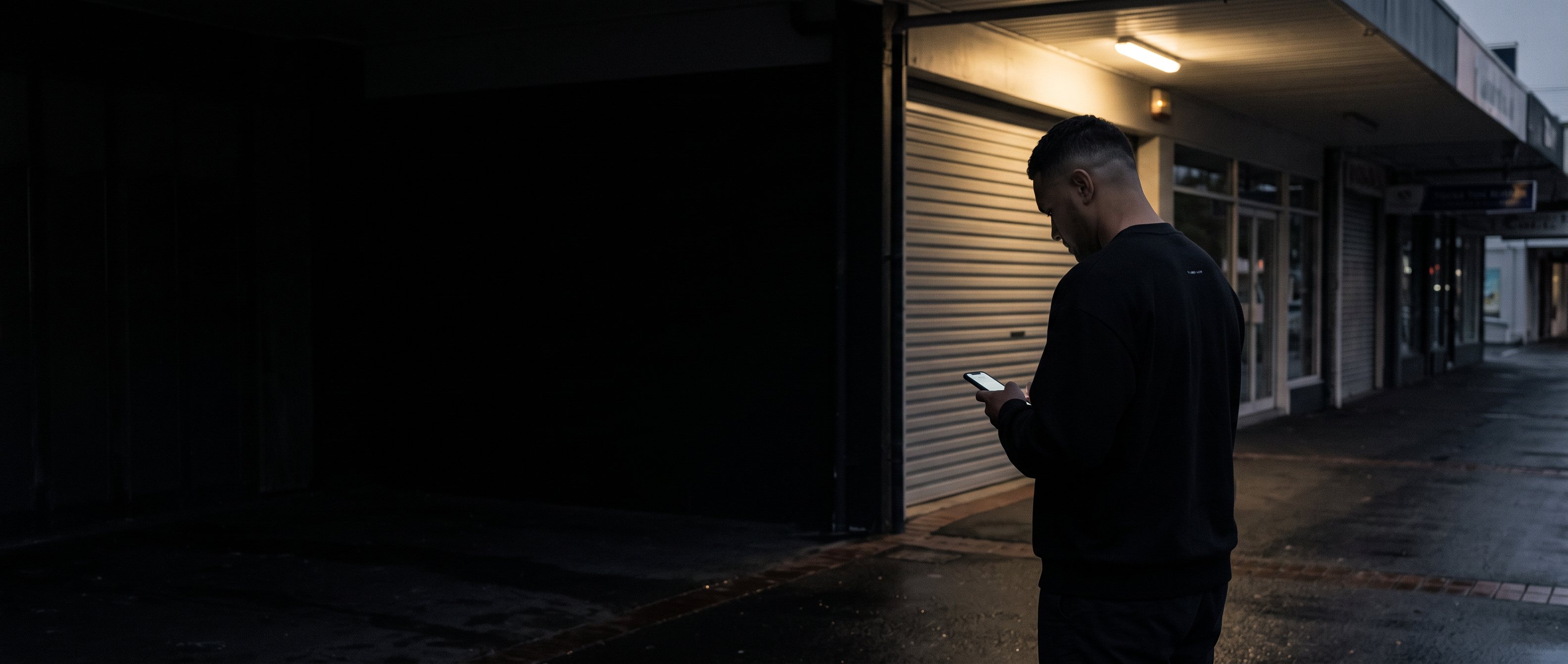 A man writing in a notebook by a window at dusk, back to camera.