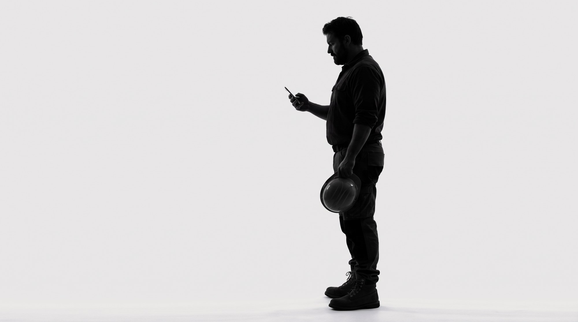 Silhouette of a trade business owner reading his phone, hard hat in hand.