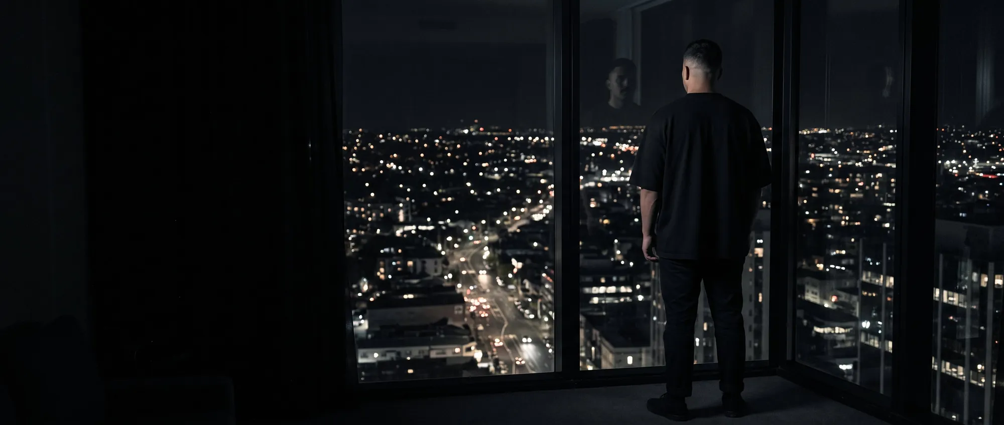 A man at a window high above a city at night, back to camera.