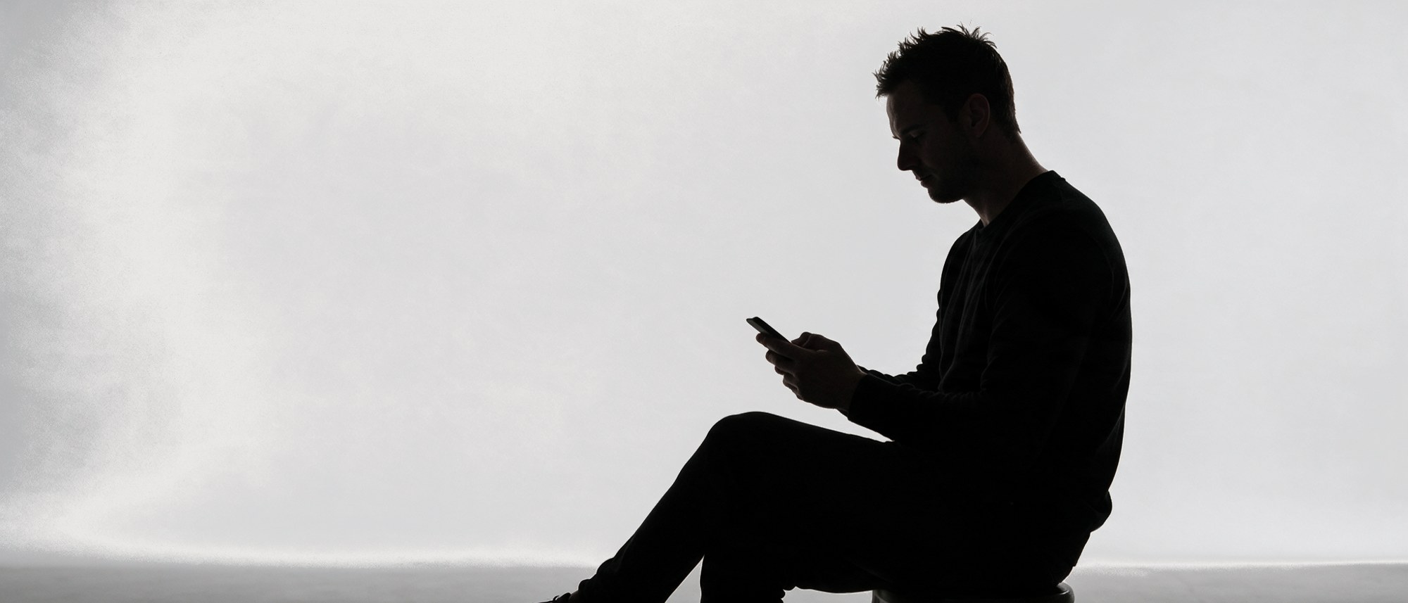Silhouette seated, scrolling a phone.