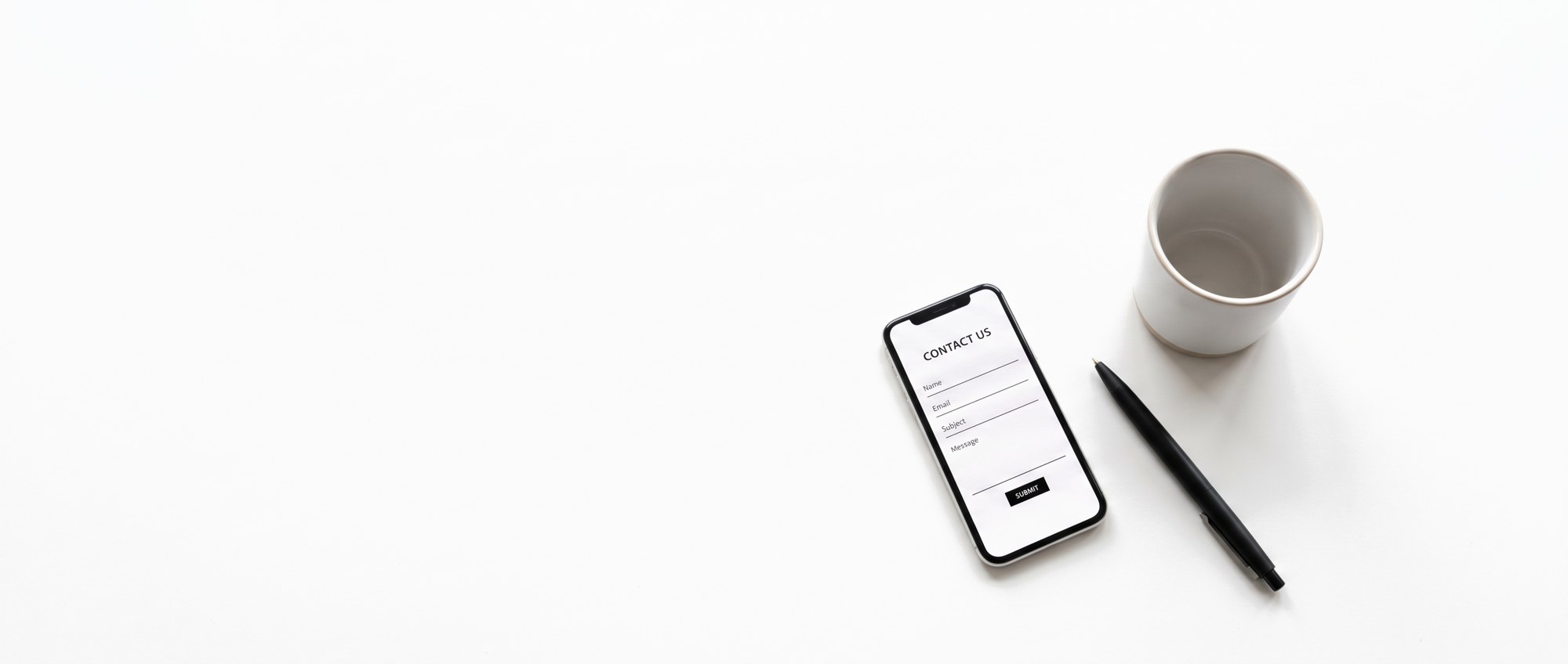 A phone showing a contact form beside a pen and a cup.