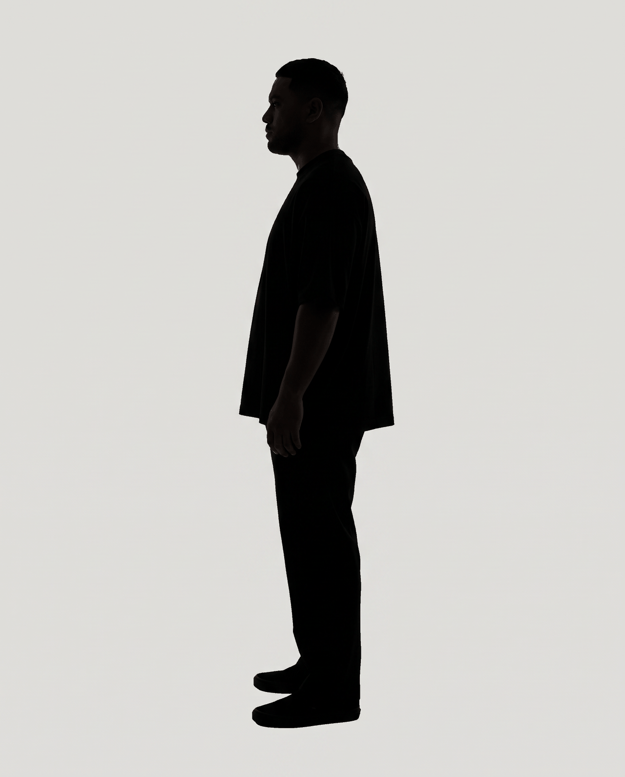Dark silhouette of a man standing in profile, arms at his sides, on flat grey.